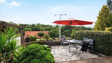 A patio with stone flooring, a red umbrella, and outdoor furniture.