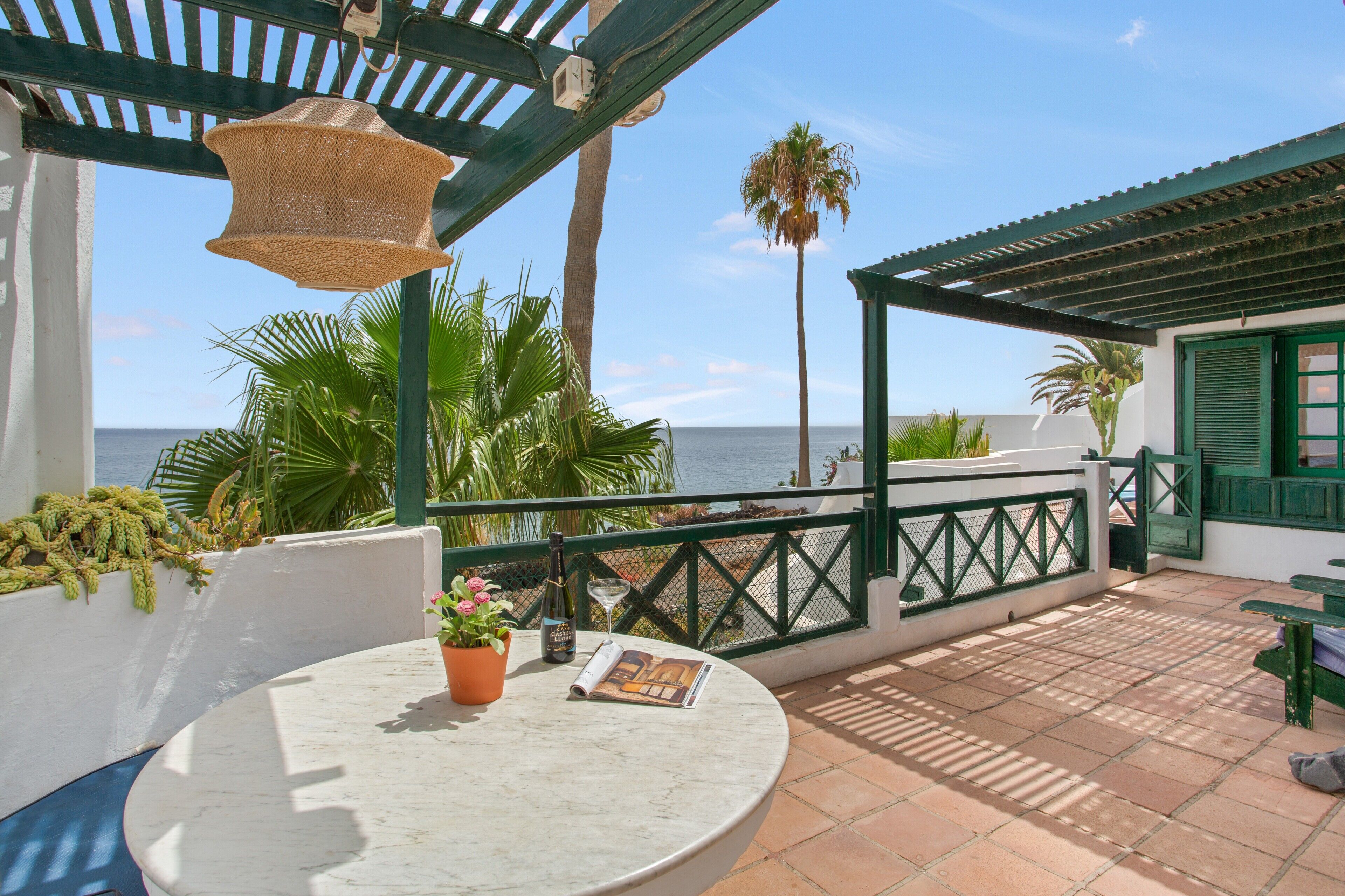 A terrace with a table, a bottle, and a book, overlooking the sea.