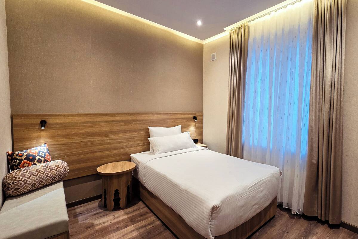Ein Hotelzimmer mit einem großen Bett, einem hölzernen Kopfteil, einem Nachttisch, einem kleinen runden Tisch und einem gemusterten Kissen.