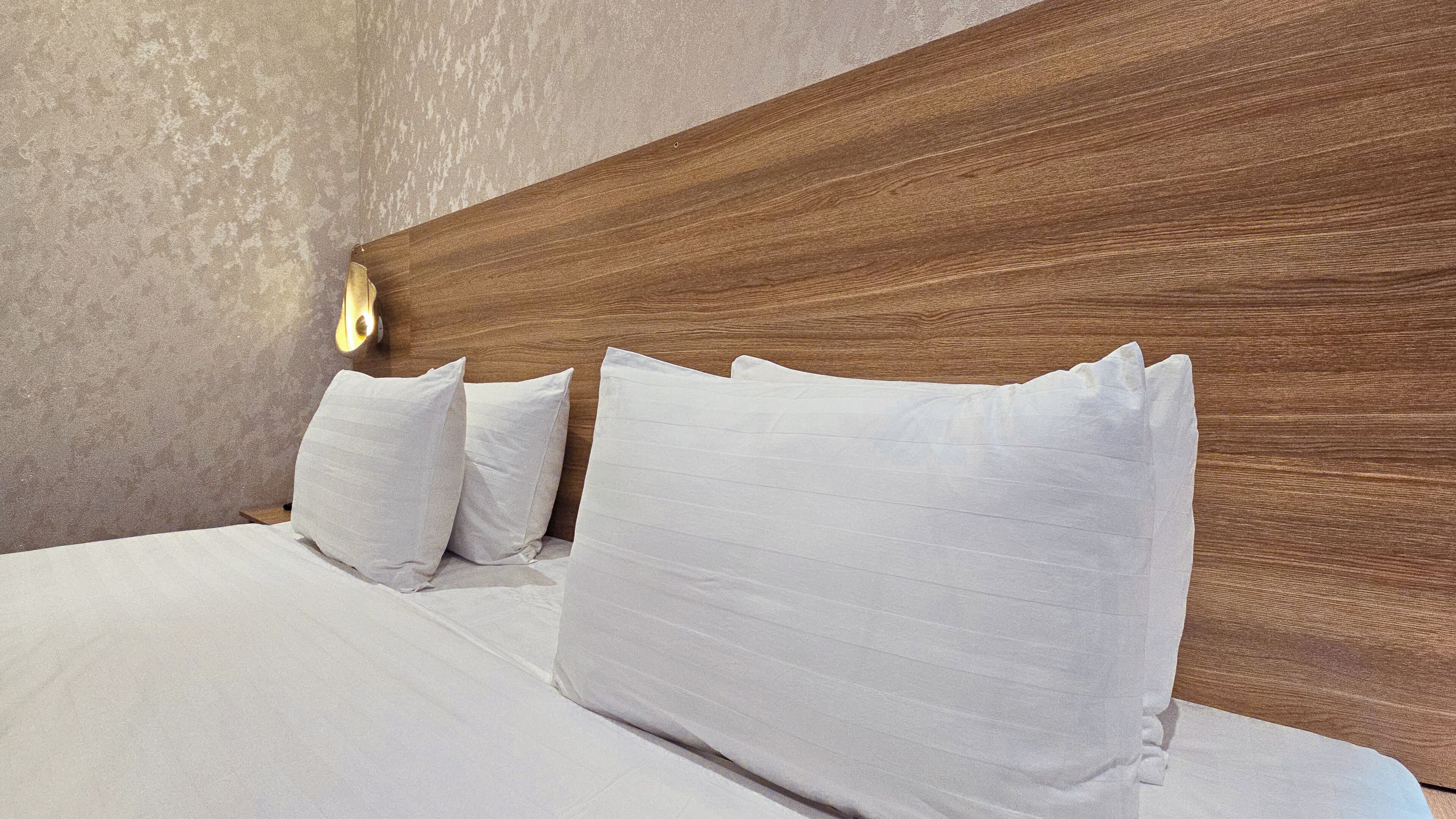 Un letto con lenzuola e cuscini bianchi, una testiera in legno e una parete strutturata.
