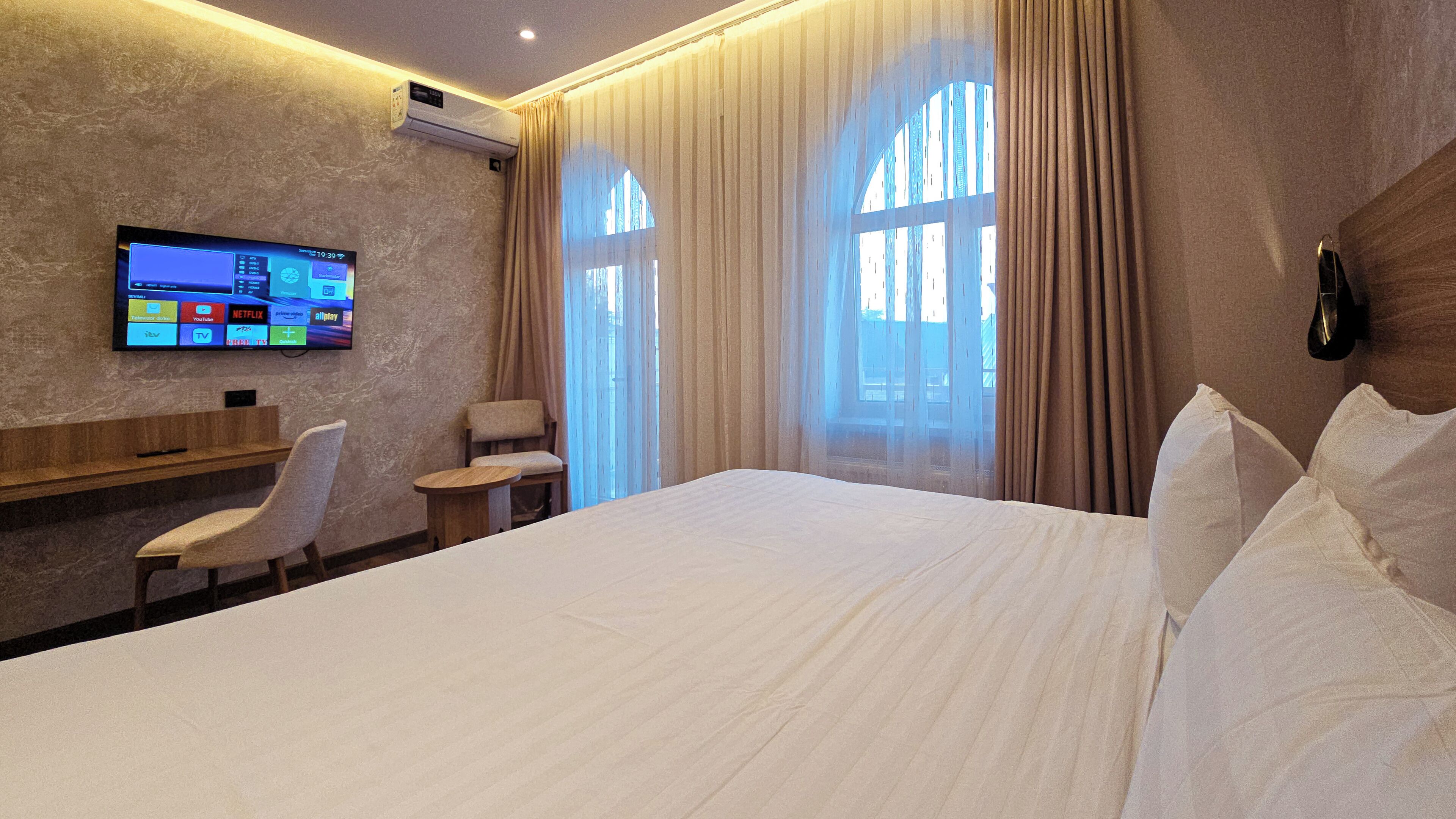 Ein Hotelzimmer mit Bett, Wandfernseher, Schreibtisch und Stuhl.