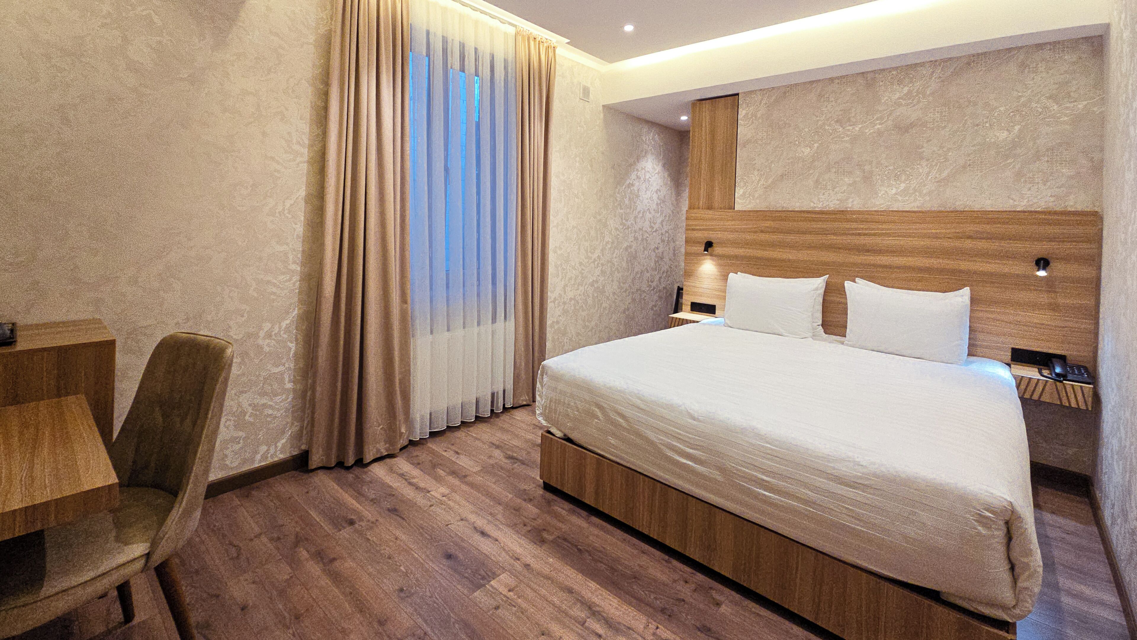 A hotel room with a large bed, wooden headboard, a desk, and a chair.