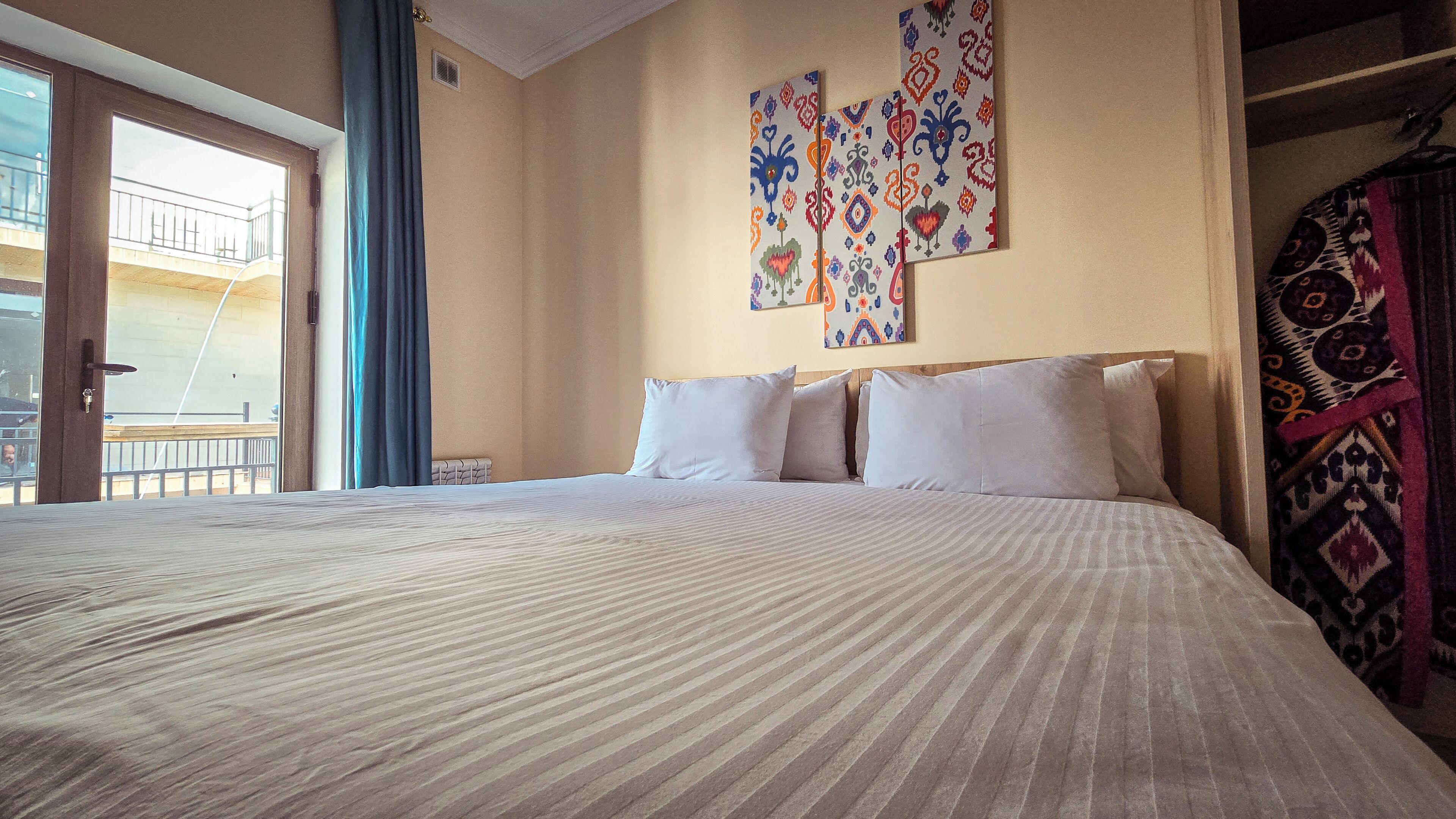 Une chambre d’hôtel avec un grand lit, une vue sur le balcon extérieur et un mur décoré d’œuvres d’art colorées.