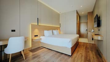 A modern hotel room with a large bed, bedside tables, a desk, and a TV.