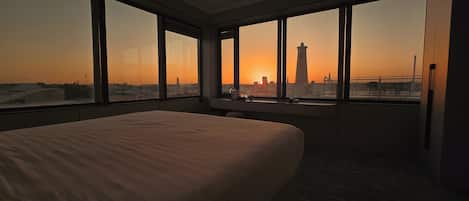 Une chambre d’hôtel avec un grand lit, un bureau et une vue sur les toits de la ville au coucher du soleil.