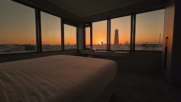 Habitación de hotel con una cama grande, un escritorio y vistas a la silueta urbana al atardecer.