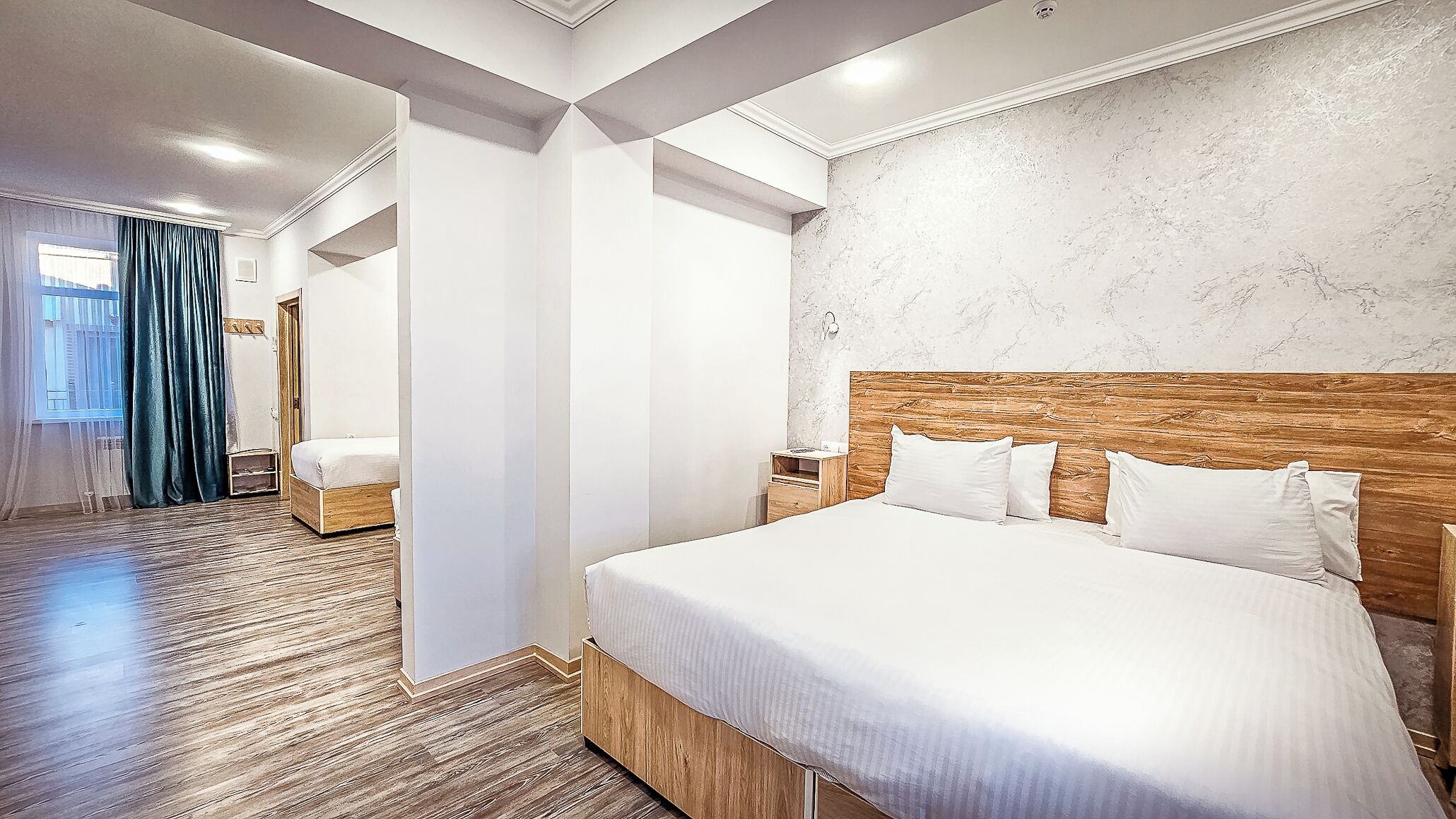A modern hotel room with a large bed, wooden headboard, marble wall, and a wooden floor.