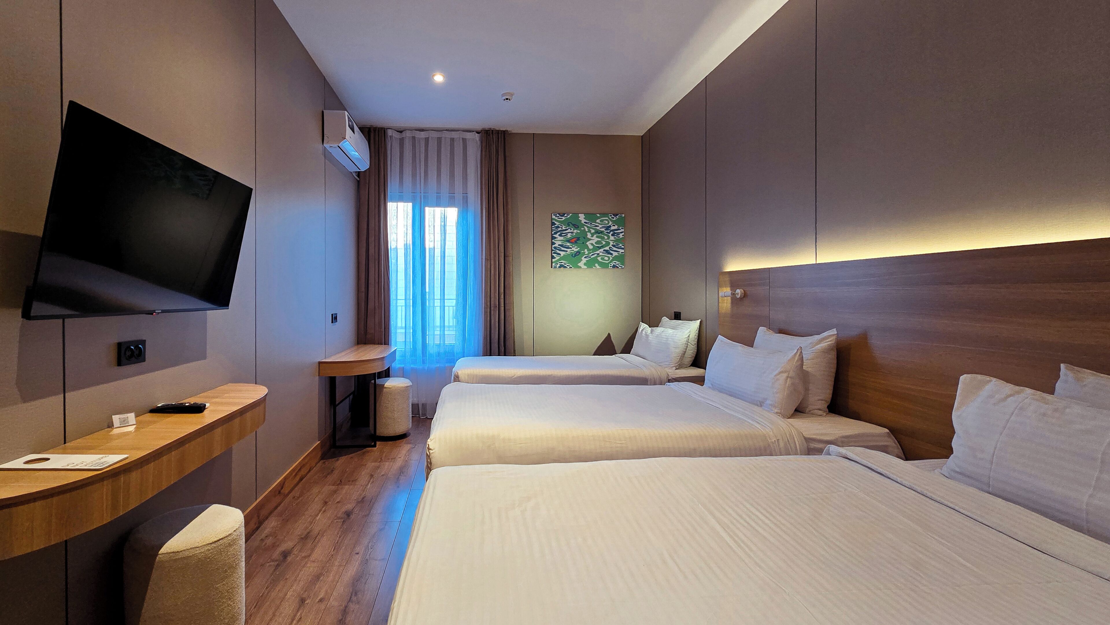 A hotel room with two beds, a TV, a desk, and a window with curtains.