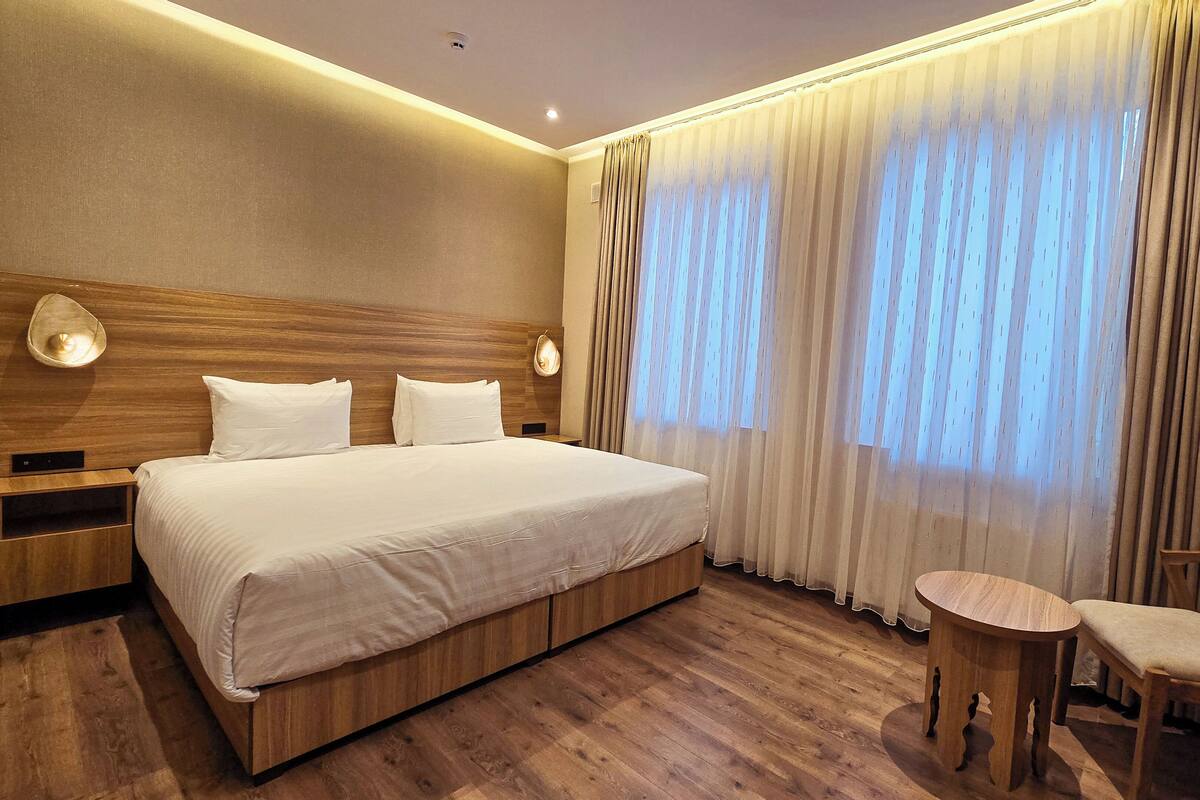 Ein Hotelzimmer mit einem großen Bett, einem Holzkopfstück, zwei Nachttischen, einem runden Holztisch und einem kleinen Tisch mit einem Stuhl.