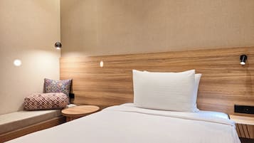 Habitación de hotel con cabecera de madera, cama con ropa blanca, mesita de madera redonda y almohada decorativa estampada.