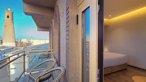 Un balcón con sillas de mimbre, una cama y vistas a una torre y al paisaje urbano.