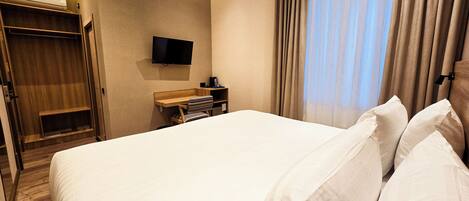 A hotel room with a large bed, a wooden desk, a television mounted on the wall, and a wardrobe.