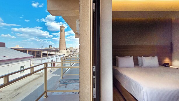Habitación de hotel con balcón que ofrece vistas a un paisaje urbano, incluyendo una torre alta.