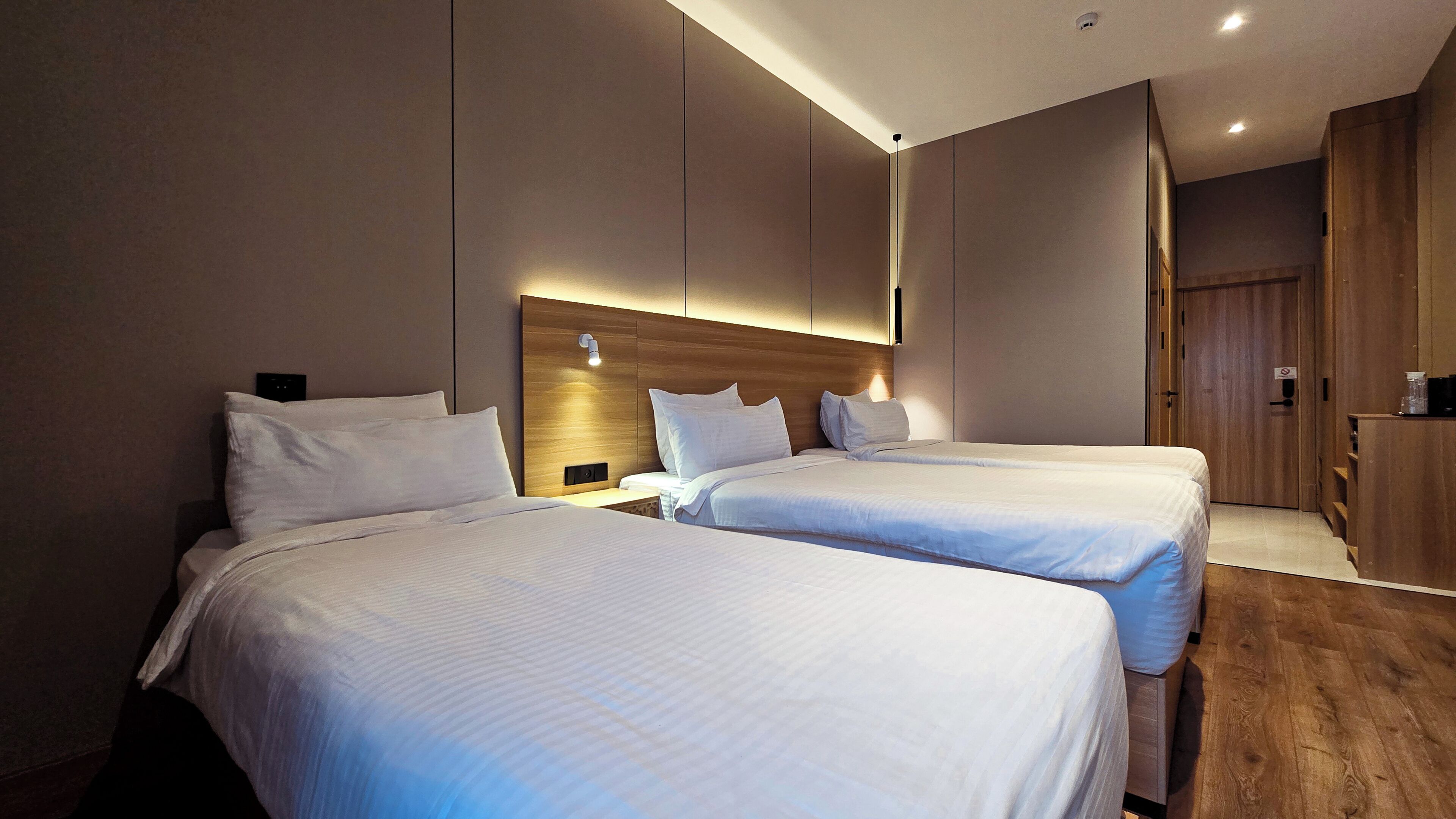 Habitación de hotel con dos camas, cabecero de madera, mesita de noche y armario.