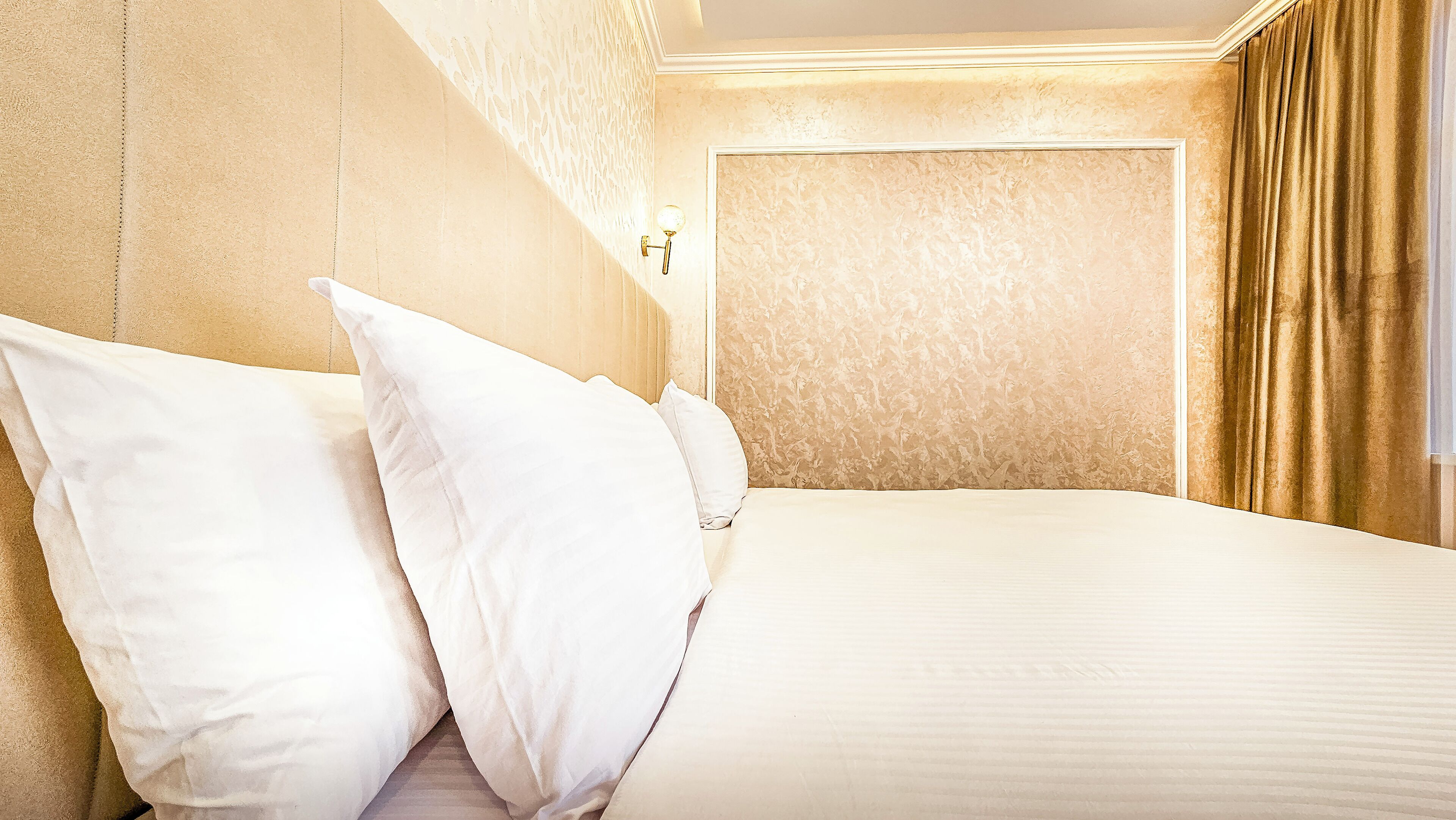 Habitación de hotel con una cama grande, almohadas blancas, cabecero, pared texturizada y una puerta con cortina.