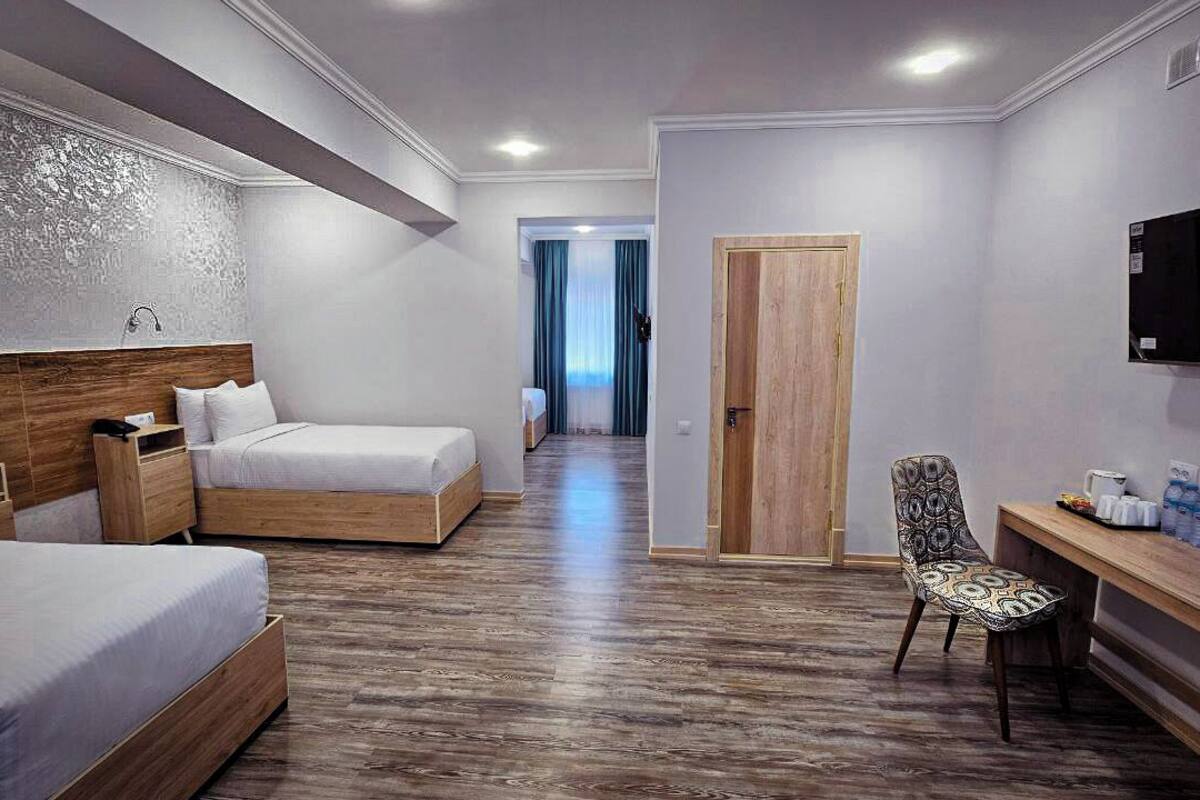 Ein Hotelzimmer mit zwei Betten, einem Schreibtisch, einem Stuhl, einem Fernseher und einer Holztür.