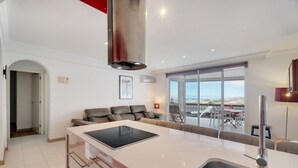 A modern kitchen with a large island, a stainless steel range hood, and a view of the outdoors.