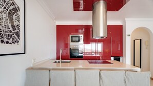 A modern kitchen with red cabinetry, a stainless steel range hood, and a bar area with four stools.