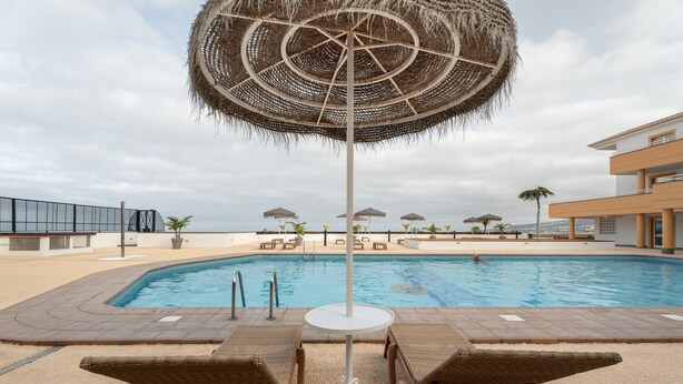 A pool area with lounge chairs, a central umbrella, and a view of the pool.