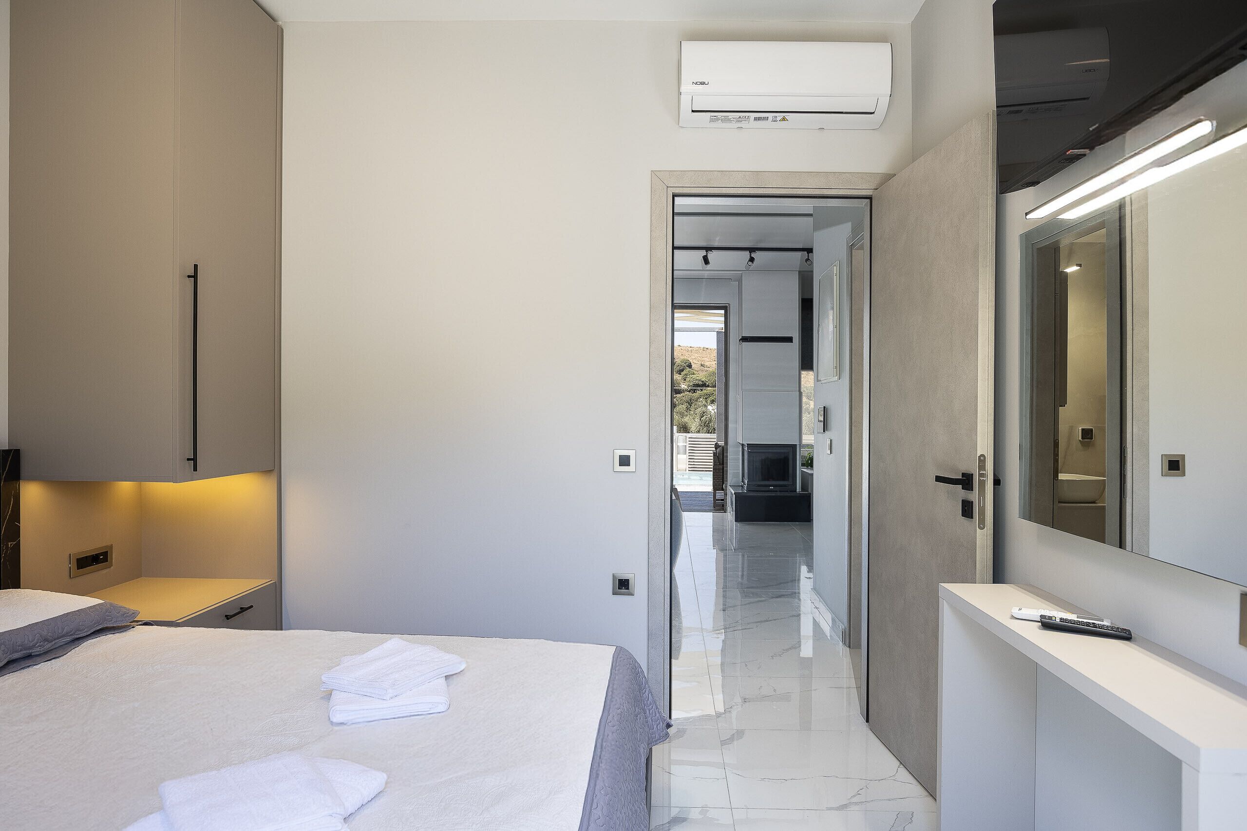 A modern bedroom with a bed, a bedside table, a mirror, and an air conditioning unit.