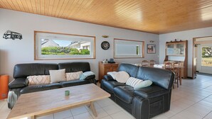 A living room with two black leather sofas, a wooden coffee table, and a dining area with a wooden table and chairs. - Holiday Home 'Villa Timao Plage' with Sea View, Private Terrace and Wi-Fi (Batz-sur-Mer)