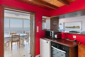 A kitchen with a view of the sea, a dining area with chairs, a small refrigerator, and a microwave. - Holiday Home 'Villa Timao Plage' with Sea View, Private Terrace and Wi-Fi (Batz-sur-Mer)