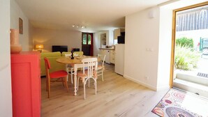 Een ruimtelijk ingerichte leefruimte met een eethoek, kitchenette en een uitzicht door een glazen deur.