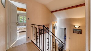 Un escalier doté d’une rampe en bois et de balustres noires, menant à une chambre à coucher avec un lit et une fenêtre.