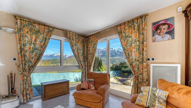 Un salon avec un canapé, un fauteuil et une vue sur les montagnes, visible à travers de grandes fenêtres.