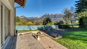 Une terrasse avec vue sur les montagnes, une clôture verte et un objet sphérique posé sur le sol.