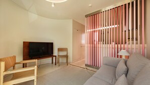Un soggiorno moderno con televisore a schermo piatto, arredi in legno, un divano grigio e un pannello separatore a righe rosa e bianche.