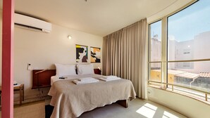 Camera d'albergo con un letto, un comodino, una lampada, una finestra con tende e opere d'arte alle pareti.