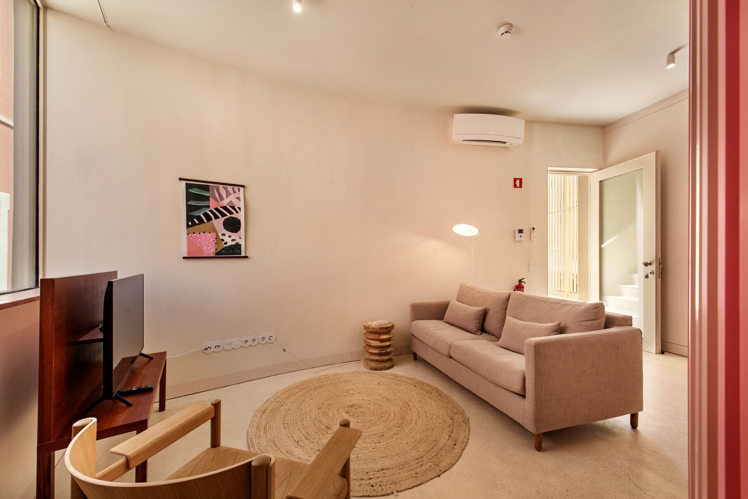 A living room with a sofa, a TV, a wooden chair, a round rug, and a wall-mounted artwork.