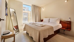 A hotel room with a large bed, a bedside table with a lamp, a mirror, and a window with curtains.