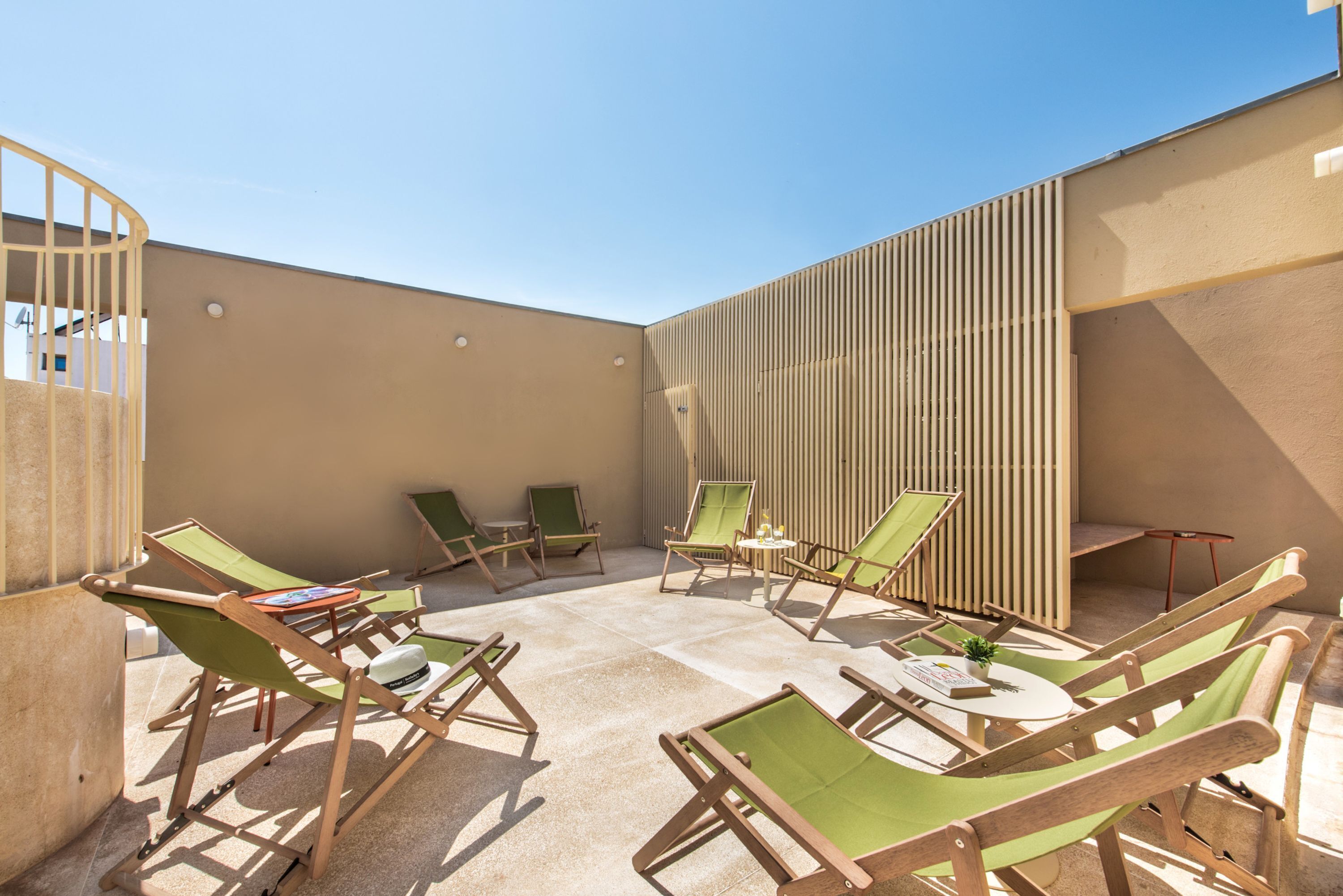 Zona relax all'aperto illuminata dal sole, con poltrone da lounge in legno e un tavolino, circondata da un muretto e un pannello verticale.