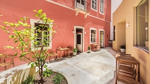 A courtyard with a red building, wooden furniture, and potted plants.