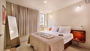 Ein Hotelzimmer mit Bett, Nachttisch, Spiegel und einem Fenster mit Vorhängen.