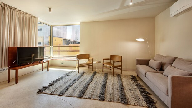 Ein modernes Wohnzimmer mit einem Flachbildfernseher, einer Couch, zwei Sessel, einem kleinen Tisch und einem großen Fenster mit Blick auf die Stadt.
