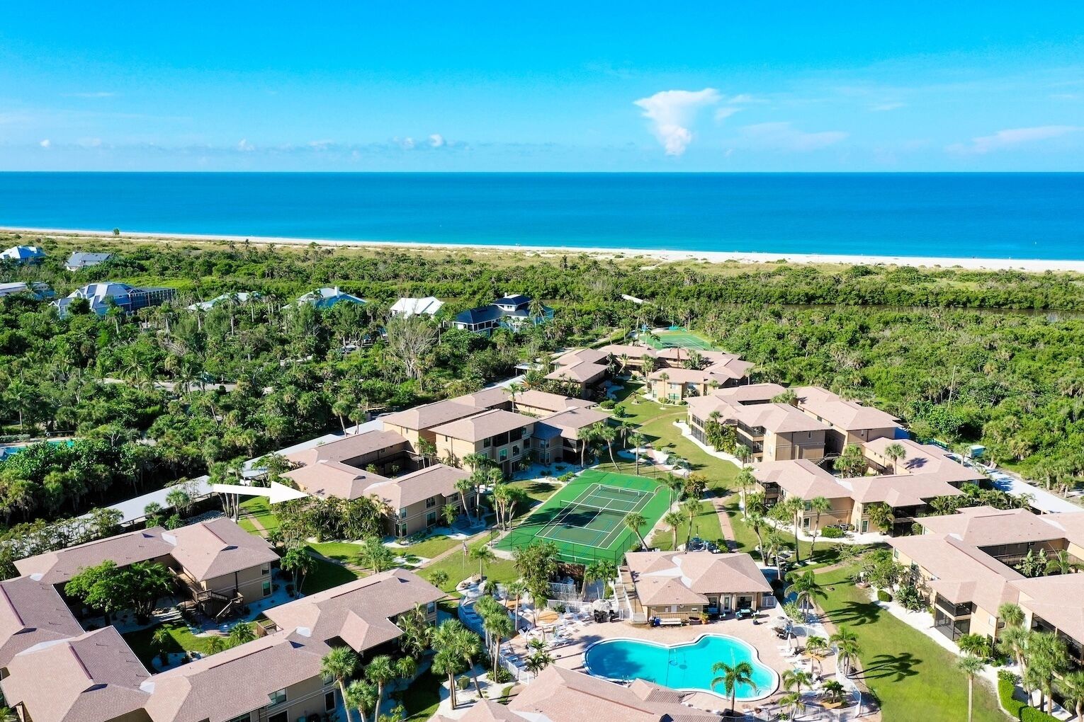 Un resort con varias construcciones, una cancha de tenis, una piscina y vista al mar.