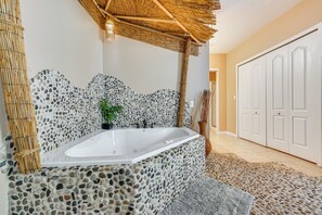 Un baño con pared de mosaico de piedra, una bañera y techo de bambú.