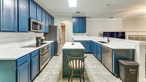 A modern kitchen with blue cabinets, a central island, stainless steel appliances, and a trash bin. - DFW Sports Hub: Home w/ Pool & Hot Tub in Frisco! (Frisco)