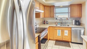 Una cocina moderna con electrodomésticos de acero inoxidable, armarios de madera, una ventana y piso de baldosas.