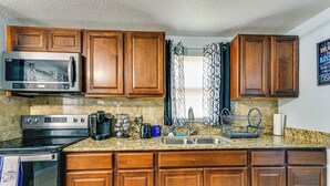 A kitchen with wooden cabinets, a stainless steel microwave, a stove, a sink, and a window with patterned curtains. - 7 Mi to Busch Gardens: Tampa Gem w/ Yard! (Tampa)