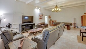 A spacious living room with a large TV, leather sofas, a wooden coffee table, and a chandelier. - Private 3-acre Retreat w/ Game Room in Bunnell! (Bunnell)