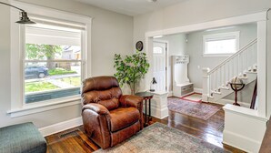 Un salon spacieux avec un fauteuil en cuir, une grande fenêtre, une plante en pot et un escalier menant à un autre niveau.