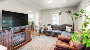 Un salon équipé d’un téléviseur à écran plat, d’un canapé, d’un fauteuil en cuir, d’une lampe sur pied et d’une grande fenêtre.