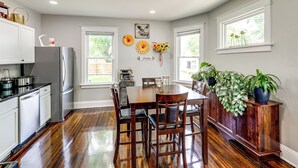 Une cuisine avec un plancher en bois, des armoires blanches, un réfrigérateur en acier inoxydable et une table à manger avec des chaises.