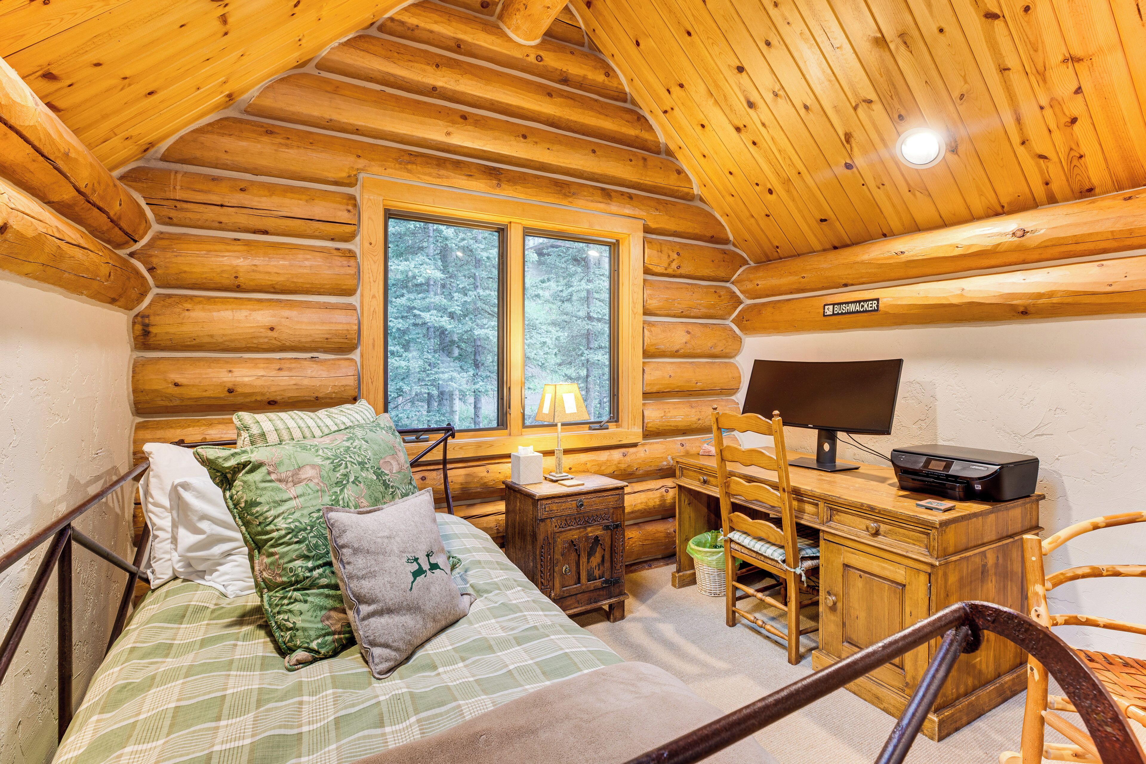 Ein Schlafzimmer in einer Blockhütte mit einem Bett, Schreibtisch, Stuhl und einem Fenster.
