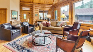 A log cabin interior with leather chairs, a round coffee table, and a large window offering a view of the surrounding forest. - Stunning Views! Ski-in/out Mountain Village Cabin (Telluride)