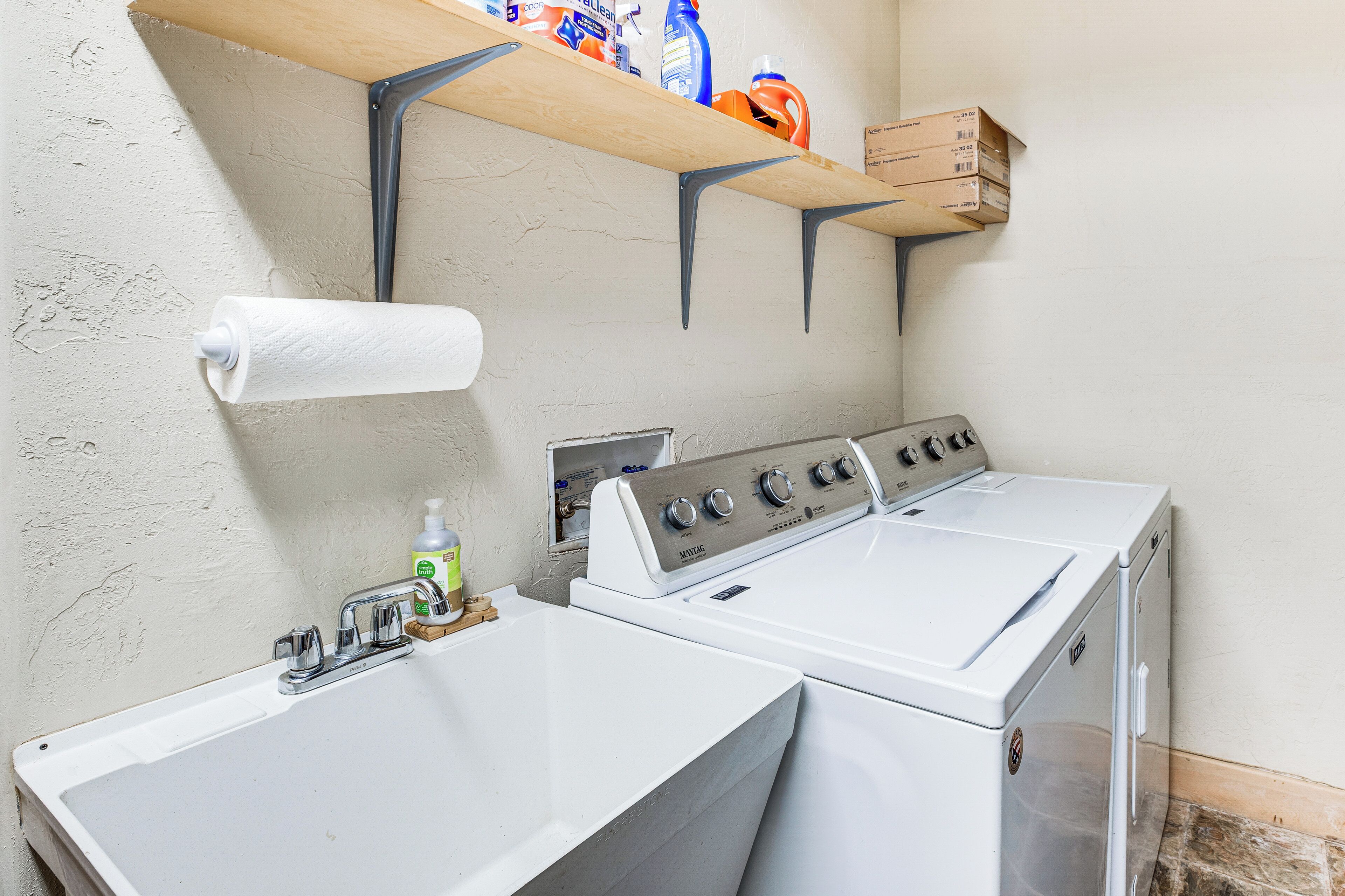 A laundry area with a washing machine and dryer, a sink, and a shelf with cleaning supplies.